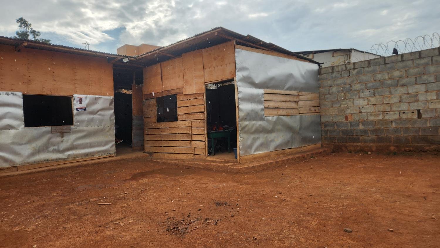 A corner of the temporary plywood and iron-sheet classrooms on red soil
