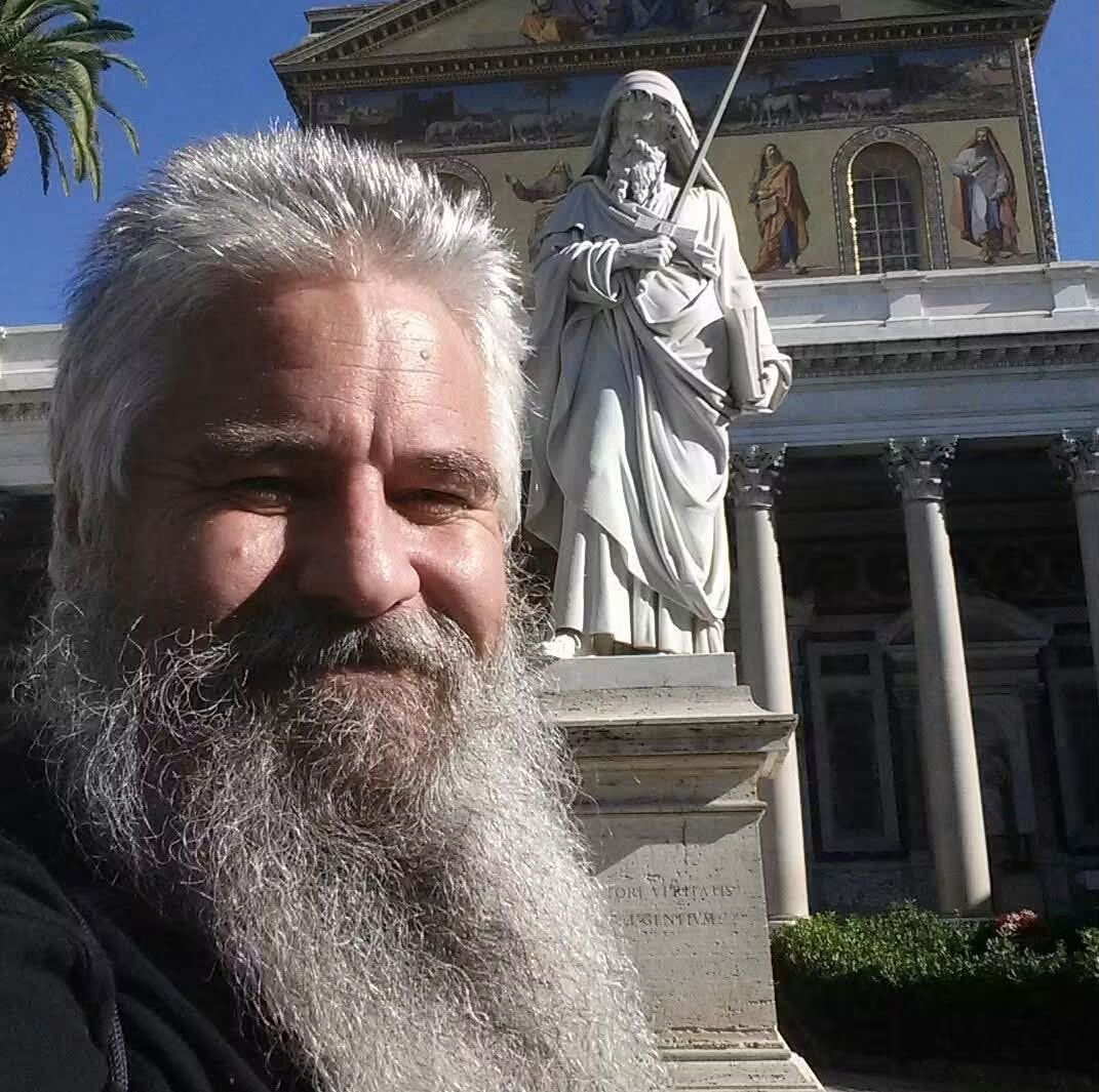 Ross Hoffman smiling beside a statue outside a church